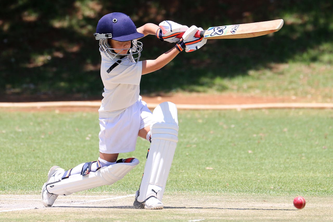 services-03 A young boy playing cricket, executing a classic sweep shot on a sunny day.